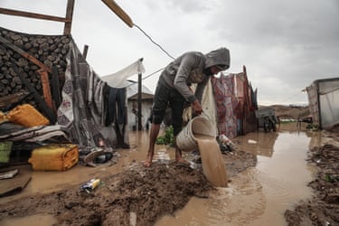 A displaced Palestinian uses a bucket to remove flood water