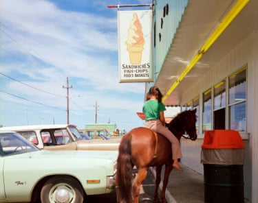 A girl sitting on a horse outside a diner, with a line of parked cars alongside