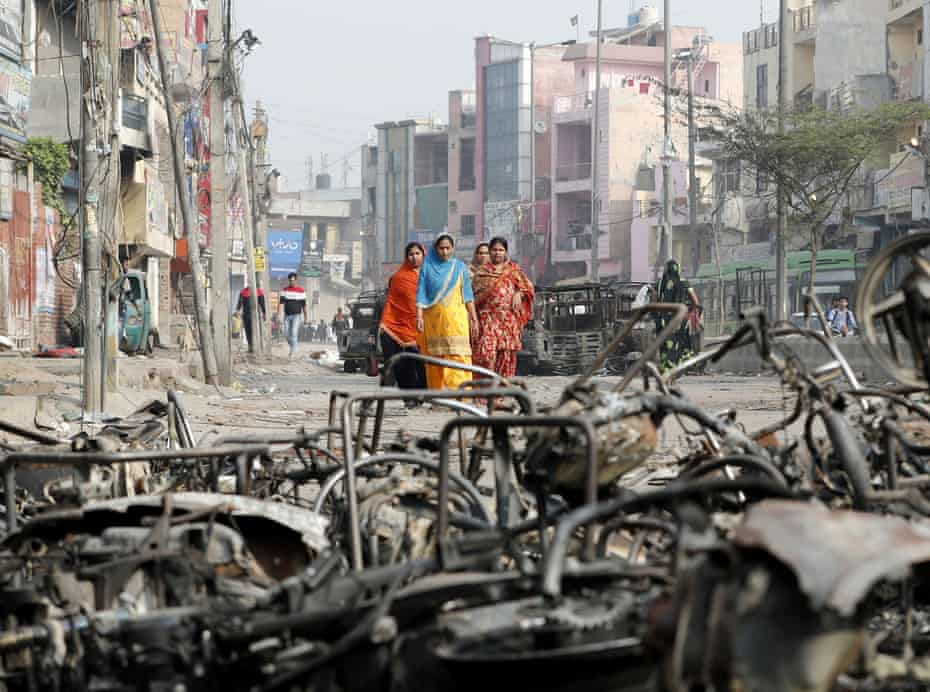 Women walk past charred vehicles in Delhi, India, 27 February