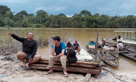 Dom Phillips and Pelado’s brother-in-law Laurindo Alves sit talking on planks of wood by the riverside