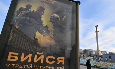 A woman walks past a poster depicting Ukrainian servicemen fighting, with a sign reading ‘Fight Together in 3rd Assault Brigade” (a brigade of the Ukrainian ground forces)