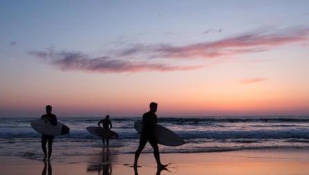 Three surfers carry their boards on the beach at sunset