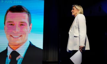 Marine Le Pen holding a document while walking past a screen showing Jordan Bardella's face