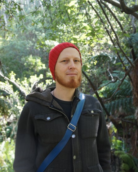 Author Wayne Marshall in a red beanie and black jacket, standing in a forest or bush-like landscape