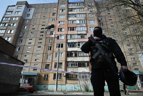 A Ukrainian policeman stands in front of residential multi-storey building damaged after a Russian strike in Kherson.