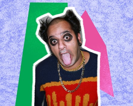 A man with hair shaved down the middle with spikes at the sides, wearing black eye make sticks out his tongue
