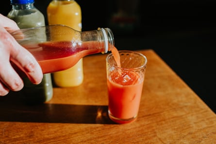A hand holds a bottle of juice and pours the contents into a drinking glass