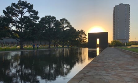 a body of water reflects a row of trees next to two buildings and the sun rising