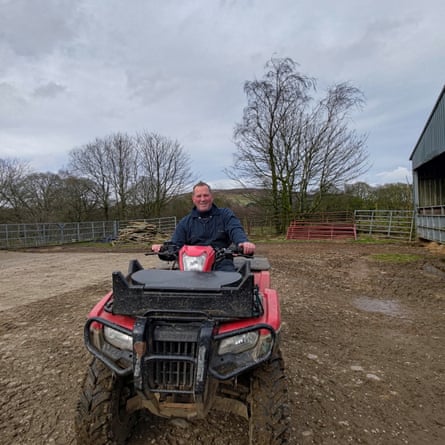 Scott Maher sits on a quad bike in a farmyard surrounded by trees yet to leaf