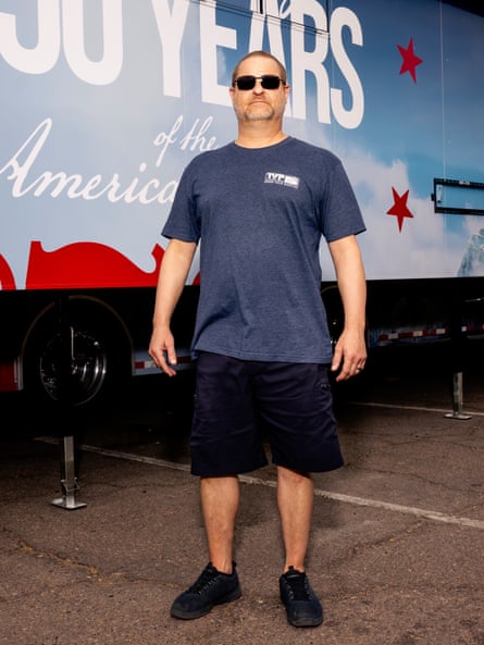 A man wearing sunglasses and a blue T-shirt stands outside of a truck