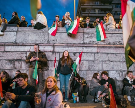 People stand around and sit down holding Hungary flags
