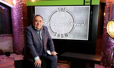 Salmond sits in a studio in front of a screen displaying the logo of his chat show, The Alex Salmond Show