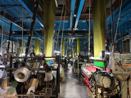 Long threads reach up to the ceiling from large machines in a large factory room
