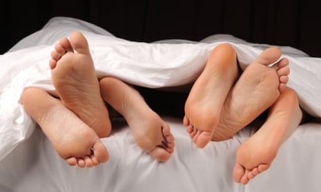 Three pairs of feet poking out of bed from underneath a duvet.