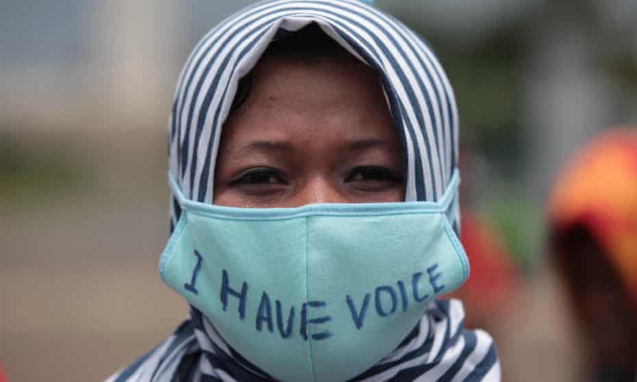 A female Indonesian human right activist in Jakarta wears a hijab and a large nose and mouth mask on which she has written 'I have voice'