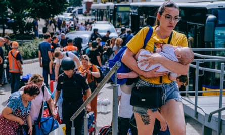 A woman holds a baby in front of crowds of people standing next to buses.