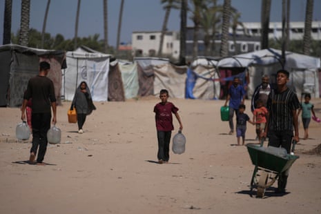 Palestinians carry containers for water at a camp for the displaced in Deir al-Balah, Gaza Strip.