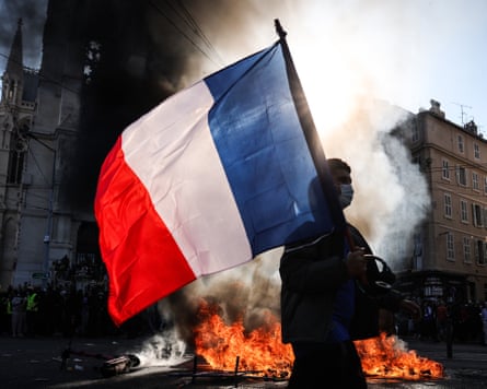 A protester waves a French national flag in front of a fire in the street