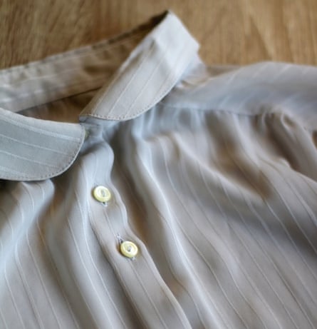 Gray striped blouse with pearl-shell buttons on wooden background. Selective focus.
