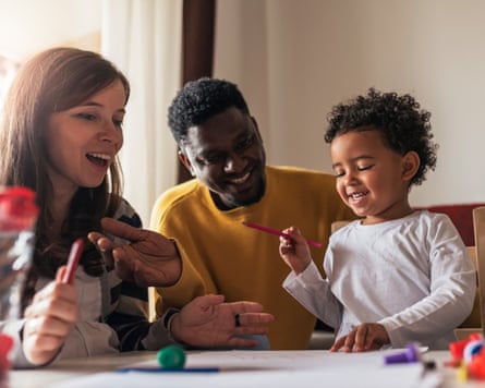 A white mother and a black father play with their child at a table in a posed photo