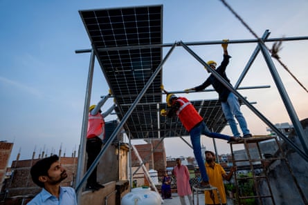 Workers install solar panels on a rooftop in India.