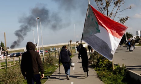 Migrants leave the refugee camp in Calais last October(one carrying the Sudanese flag).