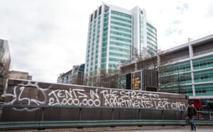 A man glances at graffiti referencing the juxtaposition between homeless people living in tents on the streets and £1m luxury apartments remaining empty.