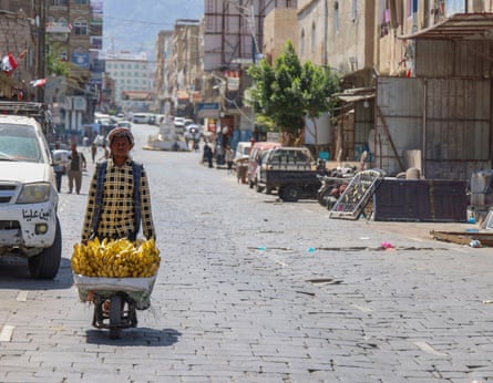 A Yemeni man pushing a wheelbarrow full of bananas down a street