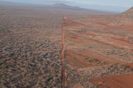 Aerial view of landscape with a clear line down the centre. On the right the land is barren and red, on the left it is green with trees.