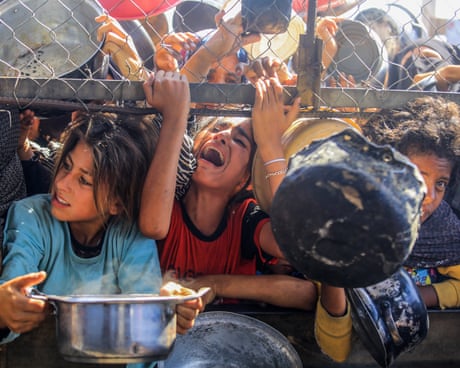 Distressed-looking children crowd an opening in a fence to receive food