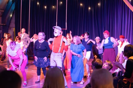 Group of people in different colourful outfits in a circus space with trapezes behind
