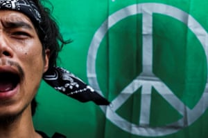 A man wearing a bandana appears to be shouting in a closeup of his face on the left side of the picture, while behind is a large CND peace sign