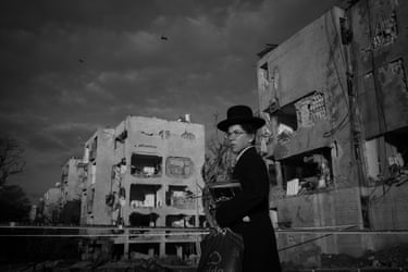 A young ultra-Orthodox Jew with a carrier bag stands amid bombed-out buildings looking to the sky