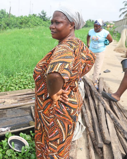 ‘The water is no longer our friend’: how dredging is pushing Lagos Lagoon towards ecosystem collapse – photo essay A woman wearing a head wrap and a patterned dress stands with her hands akimbo next to a jetty.