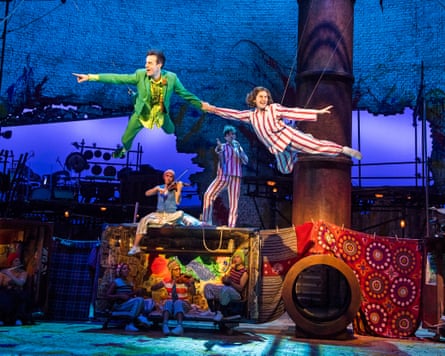 A man in a green suit and a woman in striped PJs are suspended in the air in Peter Pan on stage.