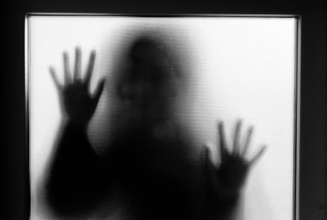 Back lit image of the silhouette of a woman with her hands pressed against a glass window.