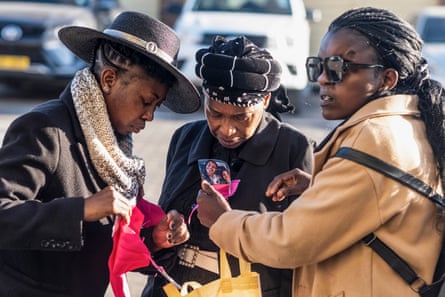 Three African women in formal dress with one holding a photograph of the dead woman and girls