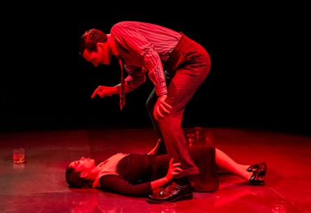 Yanexi Enriquez lying prone confronted by Alex Bhat (George Perry) lit by intense red light .
