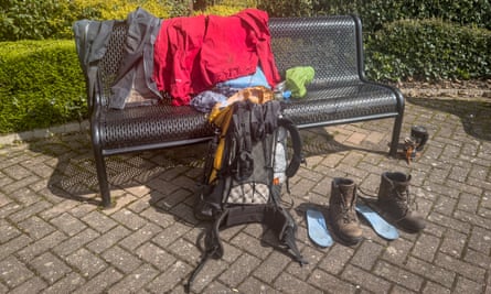 Clothes spread out on a park bench along with a rucksack and boots