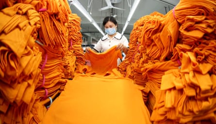A woman in a mask checks over a huge pile of folded orange t-shirts