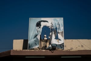 A mosque’s minaret is visible through a ripped poster of Assad