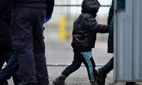 A UK immigration enforcement officer escorts a child wearing a hooded jacket