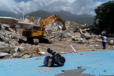 A doll lies on the ground while an earthmover clears away the rubble of a building in La Guaira.