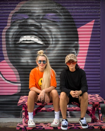 Sam and Aish Bell Doughty, in casual clothes and sunglasses, sitting on a picnic table outside House of Wingz.