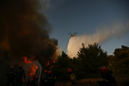 A firefighting helicopter drops water over a forest where a wildfire is burning