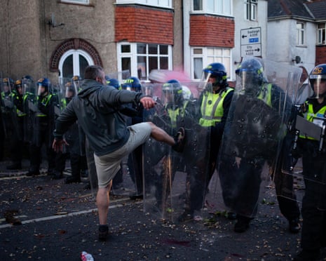 A man kicks towards a line of riot police holding shields during a street confrontation