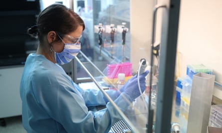 Stock image of woman with short dark hair pulled back, safety goggles and face mask holding equipment in a lab.