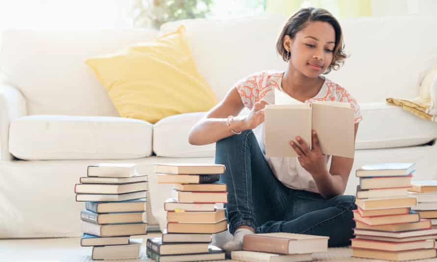 woman sitting on floor reading pile of books