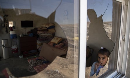 A Palestinian girl seen through the shattered window of her home after settlers attacked Al Mufakara, near Hebron.