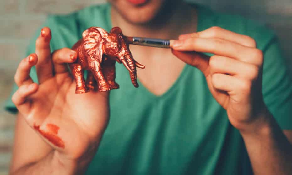 Young man painting plastic elephant figure with copper paint